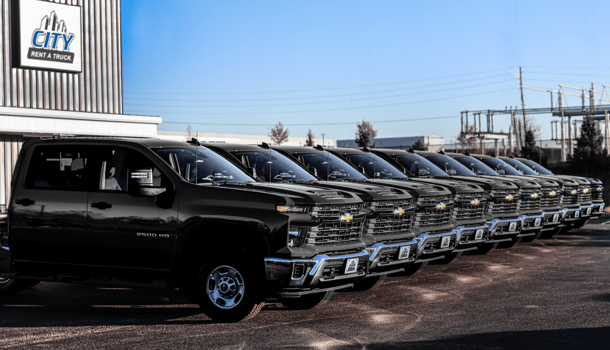 A lineup of Chevy 2500 trucks parked outdoors, ready for rental from a commercial truck rental company with locations in Kansas City, Olathe, St. Louis, Atlanta, and Houston.